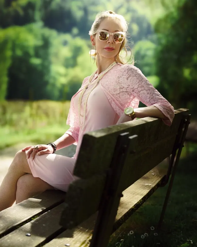 Miss Maya im rosa Spitzenkleid auf einer Parkbank, mit Sonnenbrille